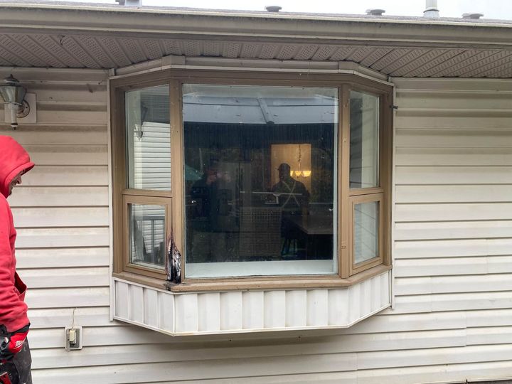 Before: Old wood-trimmed bay window on white vinyl siding before replacement