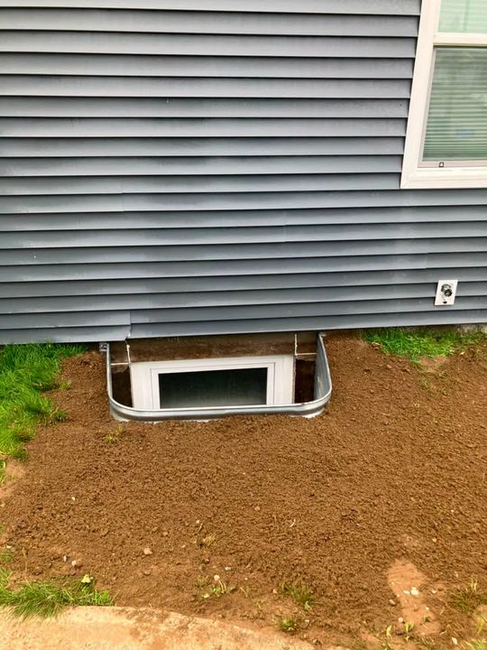 New egress window and well at grade beside grey siding