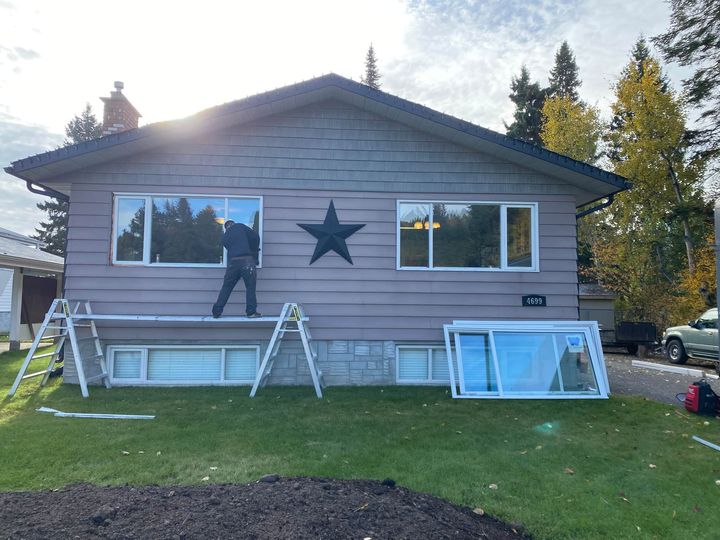 Installer setting a new front window on a grey bungalow, old frames on the lawn