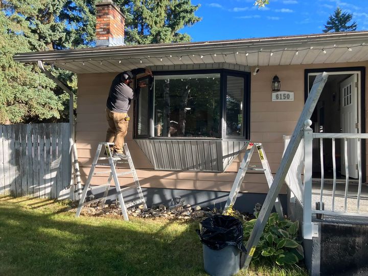 Installer removing the old front bay window on a tan bungalow